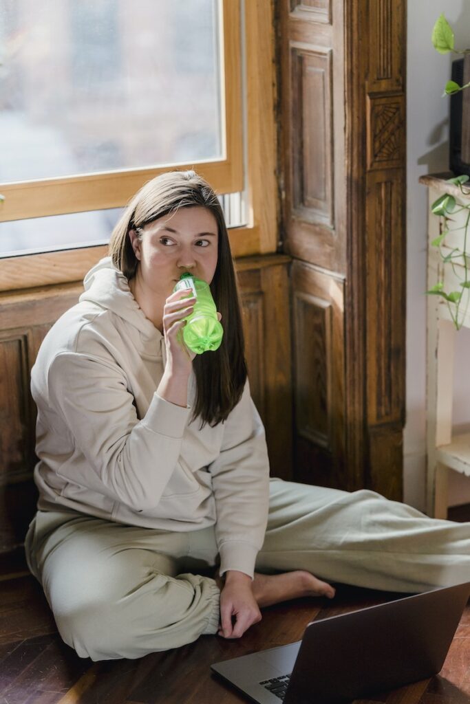 Young self employed woman drinking coke while sitting on floor and using laptop