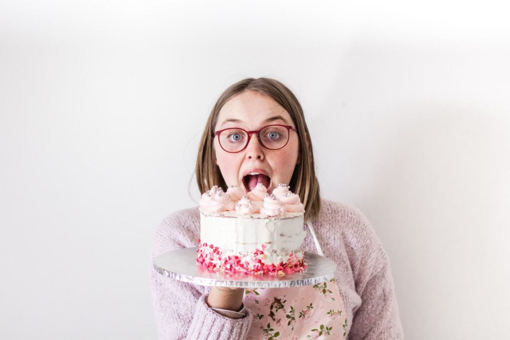 woman in gray sweater holding white and pink cake